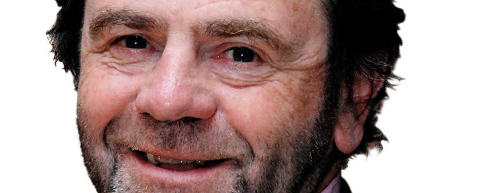 Close-up view of a smiling older man with a beard and mustache wearing a dark shirt.