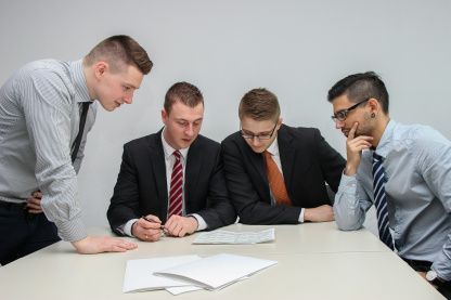 Four men in business attire discussing papers at a table in an office